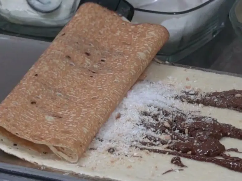 Palačinka s čokoladom i šećerom se mota na ploči aparata